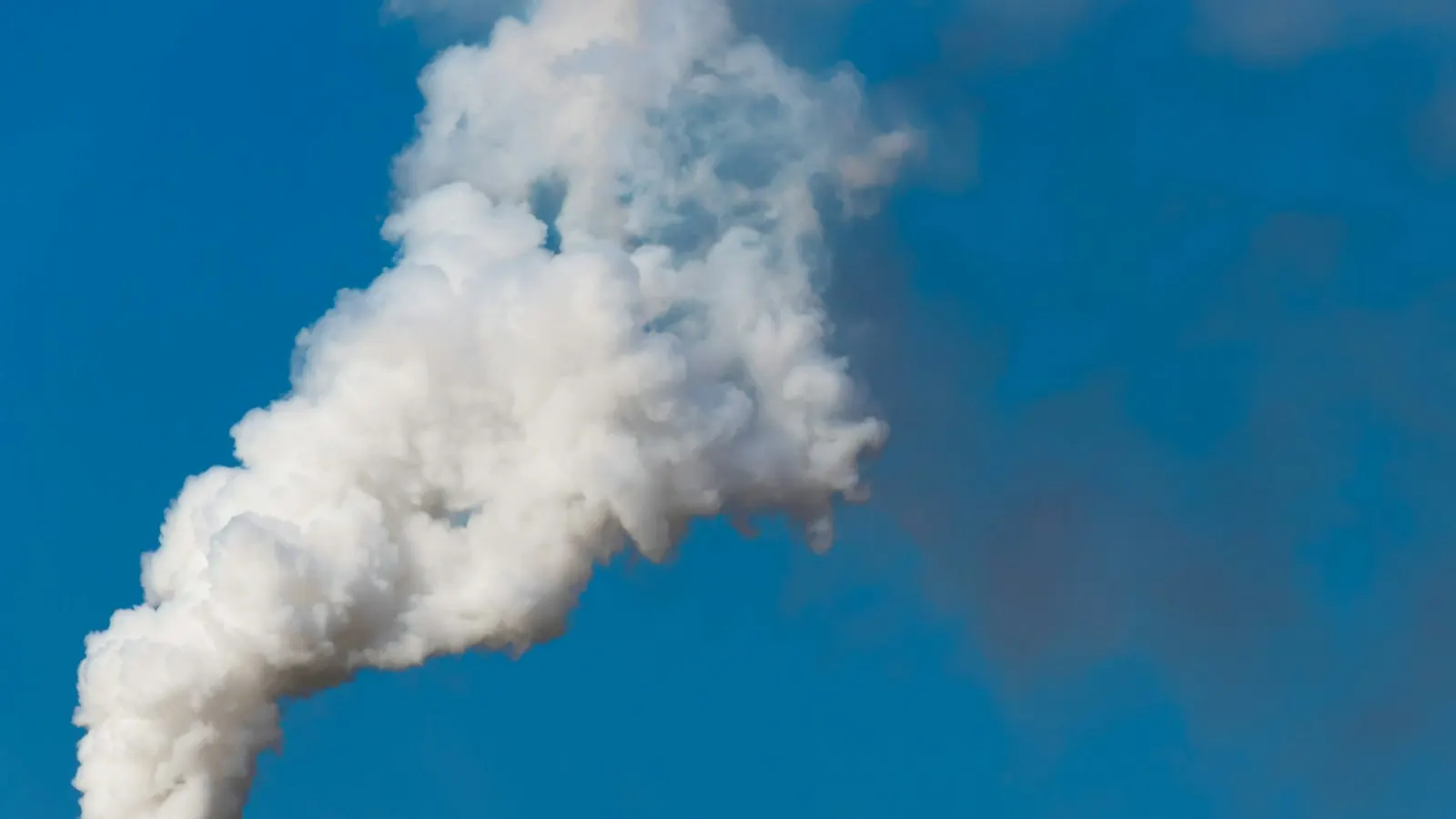 White smoke rising from an industrial chimney against a blue sky